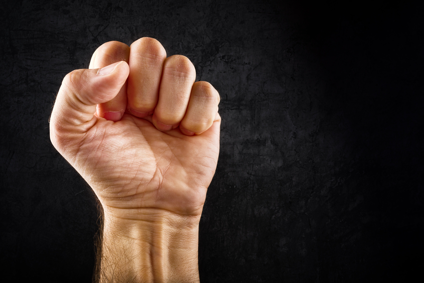 Riot protest fist raised in the air. Male clenched fist on dark grunge background.