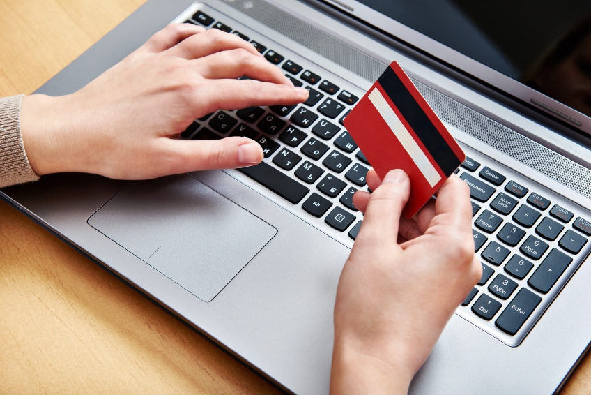 Image of a hang holding a credit card, whilst another hand hovers over a laptop keyboard ready to type. 